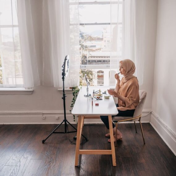 Blogger met hoofddoek werkt aan make-uplook bij raamlicht