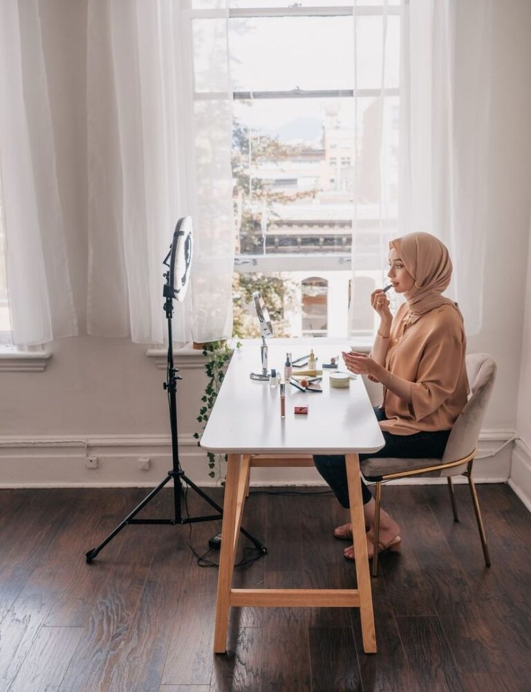 Blogger met hoofddoek werkt aan make-uplook bij raamlicht