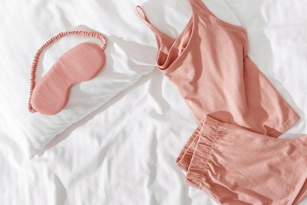 Roze nachtkleding, slaapmasker en hoofdband op wit beddengoed