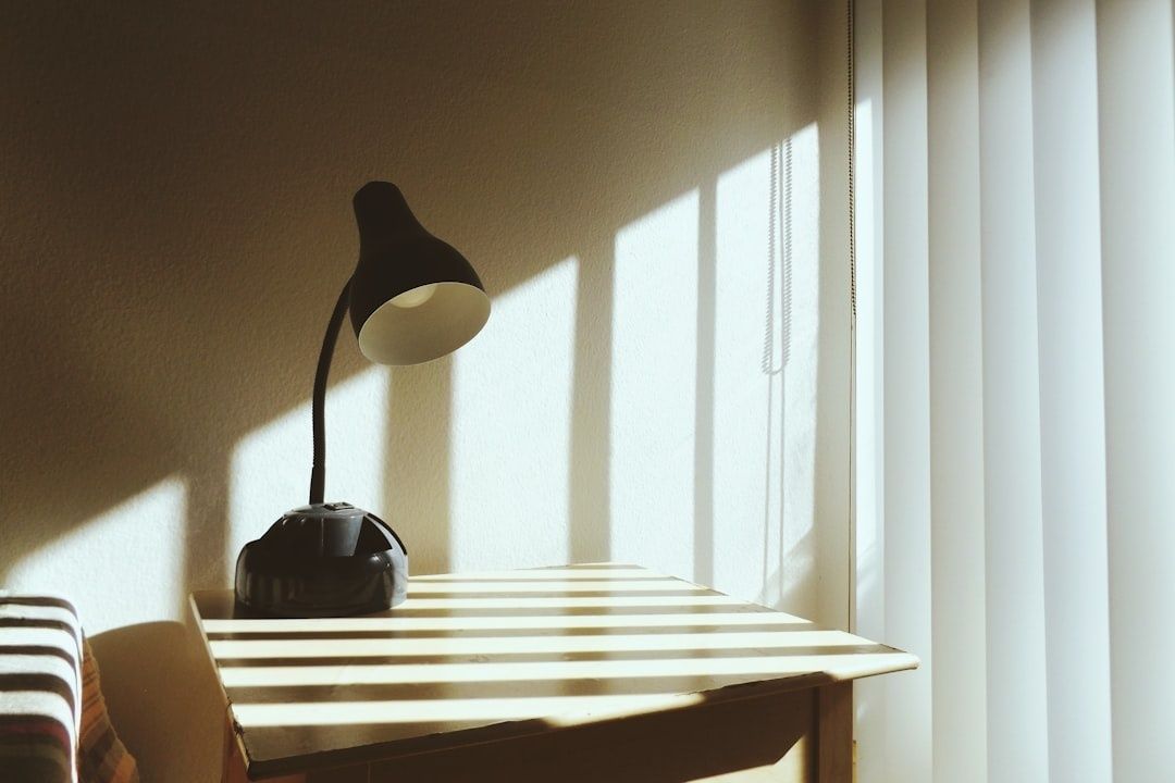 Kleine houten schrijftafel met zwarte lamp bij een zonnig raam