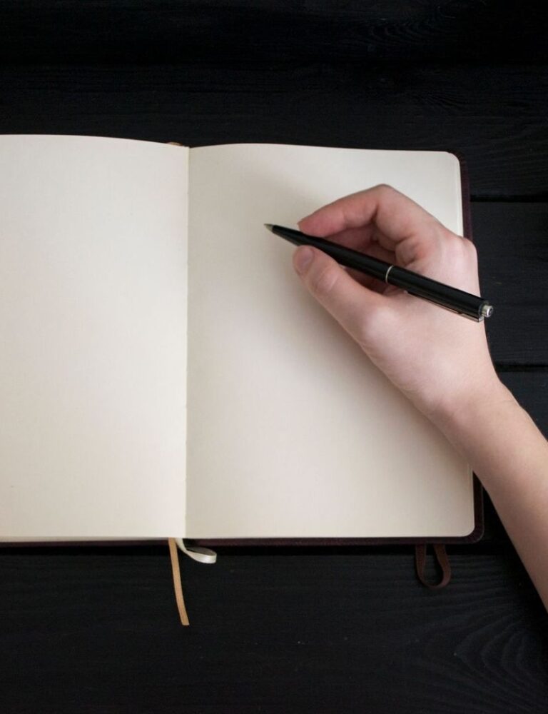 Hand schrijft met een zwarte pen in een leeg notitieboek naast koffie