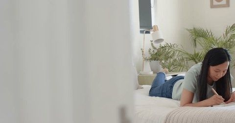 Vrouw schrijft in een notitieboek op bed in een lichte slaapkamer